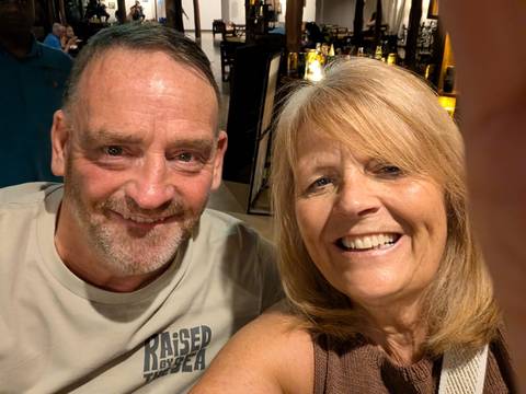       Close-up selfie of a smiling man and woman indoors under warm light.
  