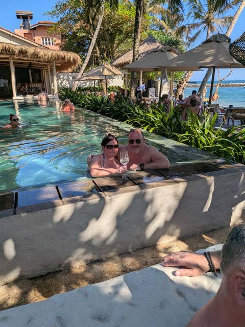       Couple enjoying wine while relaxing in a resort infinity pool with greenery around.
  