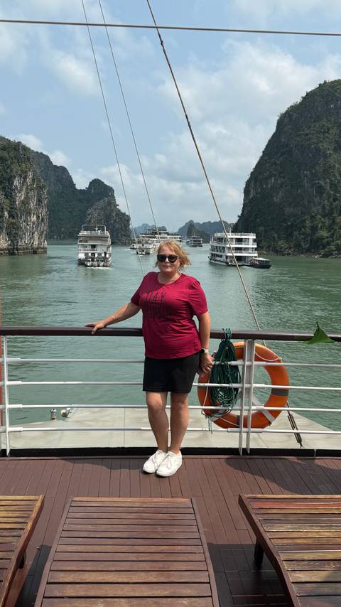       Woman poses on cruise railing with emerald waters and limestone karsts of Halong Bay behind
  