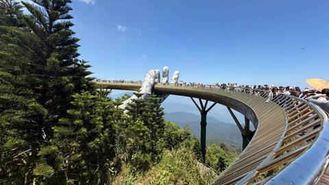      Side view of the curved Golden Bridge crowded with visitors above green forested valley
  