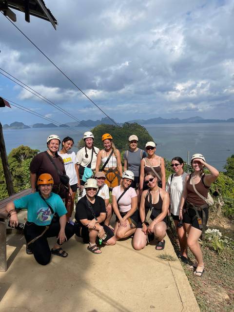       Smiling adventure group in helmets pose before island-dotted sea view on a sunny day
  
