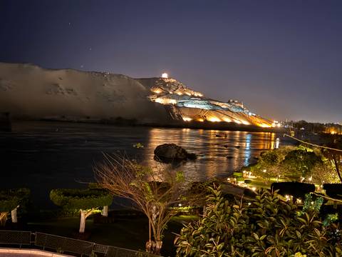       Night view of illuminated mausoleum on desert bluff reflecting across the Nile River
  