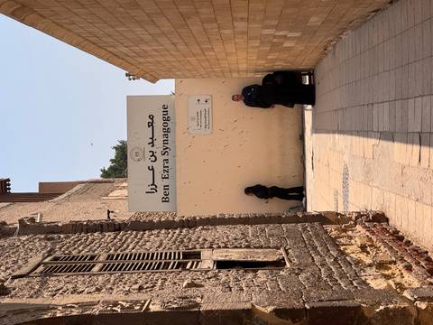       Narrow alleyway leading to the Ben Ezra Synagogue sign with a few locals standing
  