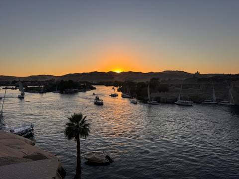       Sun sets behind low hills as feluccas sail along the shimmering Nile River
  
