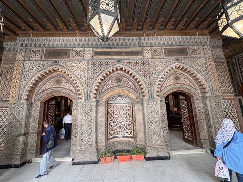       Ornately patterned facade of historic Cairo building with arched doorways and visitors entering
  