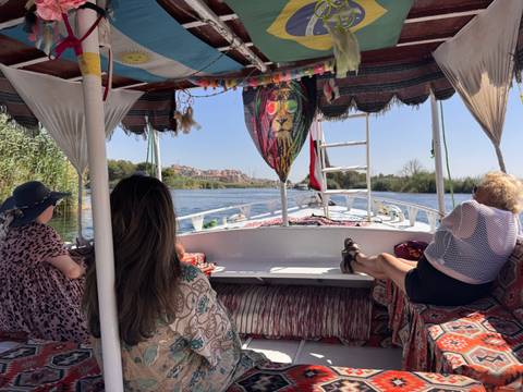       Travelers relax on cushioned benches inside a felucca cruising the Nile
  