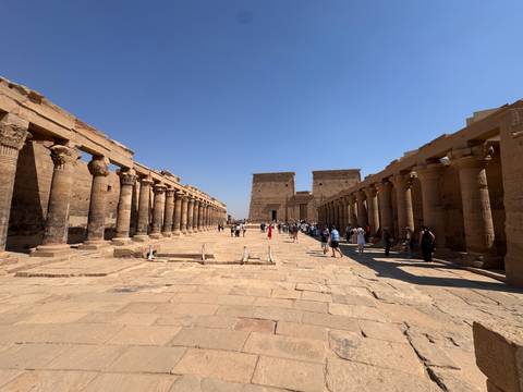       Stone colonnades flank the main axis of Philae Temple complex filled with visitors
  