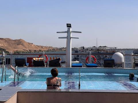       Cruise ship pool deck with guests relaxing while Nile riverbank passes by
  