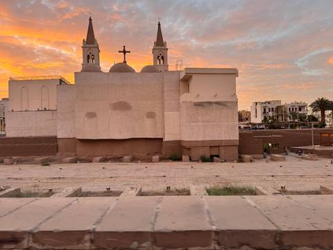       Christian church silhouette against colorful sunset sky with foreground ruins
  