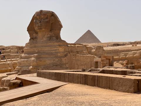       Side profile of the Great Sphinx with a pyramid rising in the desert behind
  