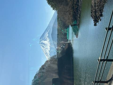       Snow-capped Mount Fuji reflected on bus window above tranquil river and forest.
  
