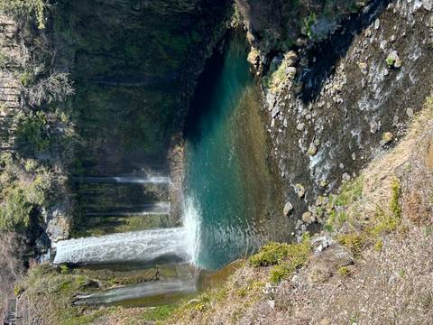       A tall waterfall plunges into a turquoise pool surrounded by moss-covered cliffs and forest.
  