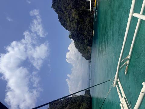       View from a bangka boat of turquoise water and green limestone islands under a partly cloudy sky.
  