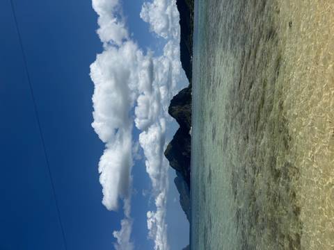       Clear shallow sea leading to dramatic green limestone islands beneath scattered white clouds.
  