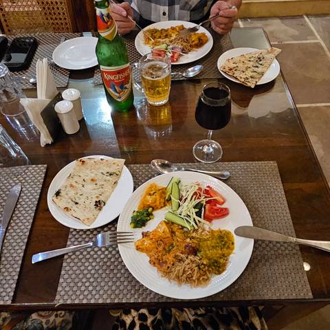       Restaurant table setting with Indian curry, naan, salad, beer and wine ready to be enjoyed.
  