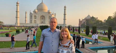       A smiling couple stands in the Taj Mahal gardens at dusk with the iconic mausoleum glowing softly behind.
  