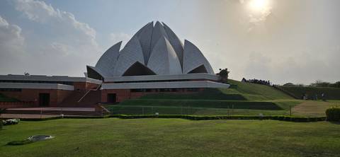       Wide ground-level shot of the Lotus Temple with manicured lawns under a hazy afternoon sun.
  