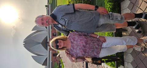       Couple poses in front of the Lotus Temple at sunset, sunlight flaring behind the structure.
  