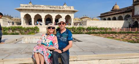       Couple relaxes on a marble ledge inside Agra Fort complex under bright blue skies.
  