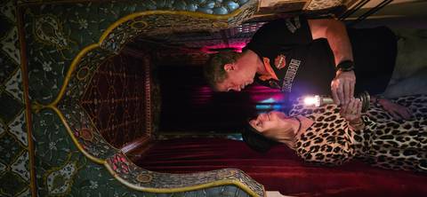       Couple shares a candle inside an ornately decorated, dimly lit palace room with mosaic walls.
  