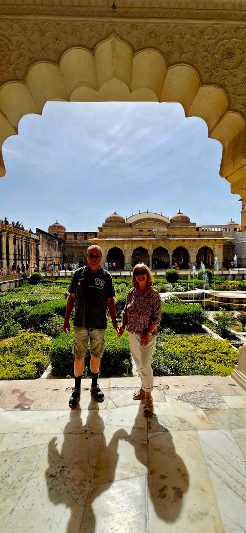       Couple holding hands in a formal Mughal garden courtyard of Amber Fort on a bright day.
  