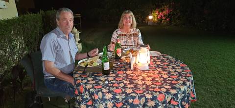       Couple enjoy an outdoor candlelit dinner on a lawn at night with patterned tablecloth.
  