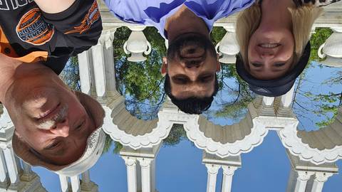       Selfie of guide and two travelers beneath white ornamental arches on a sunny day.
  