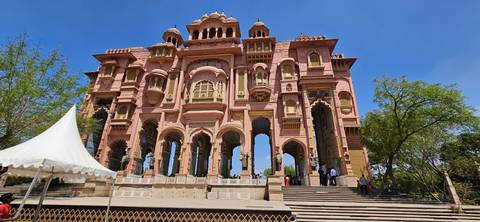      Grand pink-sandstone gateway richly carved and rising against a vivid blue sky with wide steps below.
  