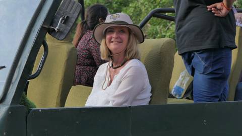       Woman in safari hat smiles from an open jeep seat during a wildlife drive.
  