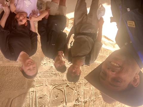       Group selfie inside an ancient Egyptian temple with sunlit relief carvings on sandstone walls.
  