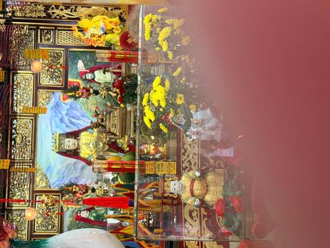       Colorful Vietnamese temple altar partially obscured by a finger in the foreground.
  