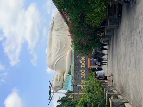       Large reclining Buddha statue towers above visitors walking through a bougainvillea-lined courtyard.
  