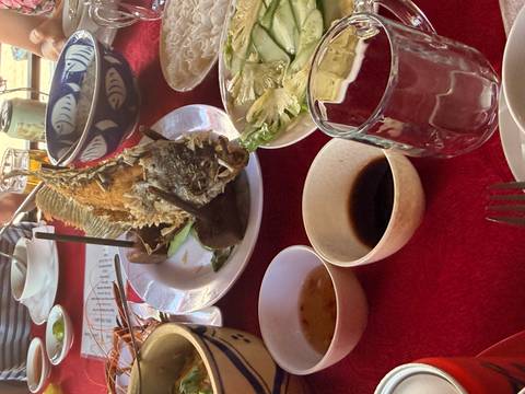       Close-up of a whole fried fish and Vietnamese side dishes laid out on a red tablecloth.
  