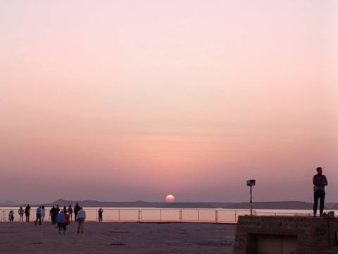       Soft pink sunset over a broad river as cruise passengers watch from deck.
  