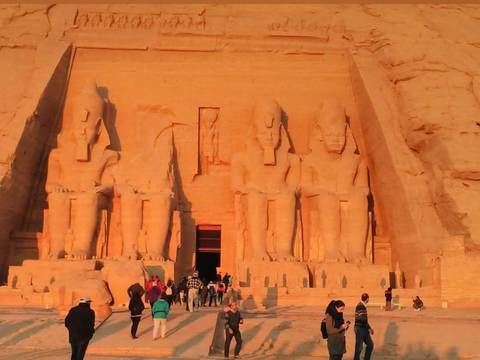       Abu Simbel temple façade bathed in warm light with small crowd at its base.
  