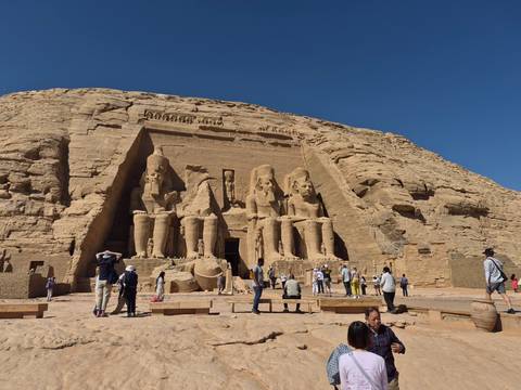       Visitors gather before the grand rock-cut statues of Abu Simbel on a clear day.
  