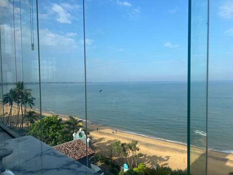       View through glass panels of a calm tropical beach and blue sea.
  