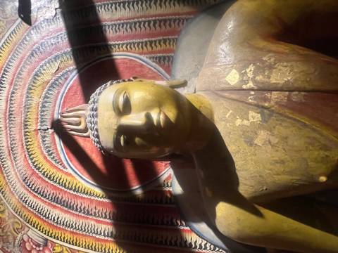       Dimly lit golden Buddha statue inside a cave temple with painted ceiling.
  