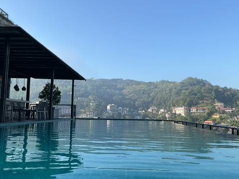       Infinity pool reflects hills and misty morning sky over a valley town.
  