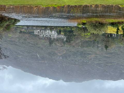       Historic stone abbey sits lakeside beneath misty mountains and waterfalls.
  