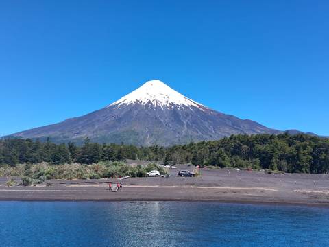       Snow-capped Osorno Volcano rises sharply above forests and a tranquil lake.
  