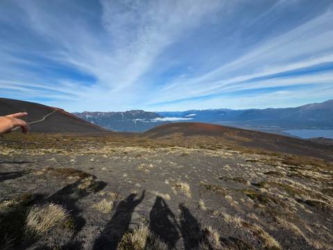      Panoramic volcanic landscape with shadowed hikers and a pointing guide in the foreground.
  