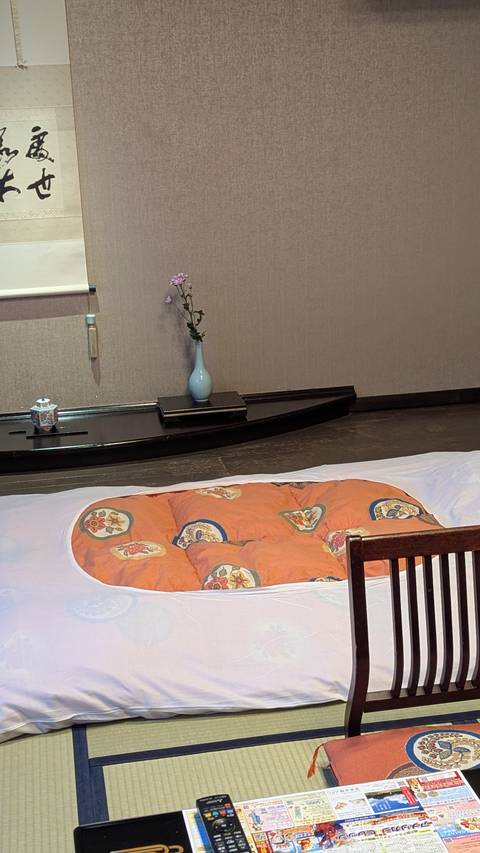       Traditional Japanese room corner with a futon laid out on tatami and a single flower in a vase as decoration.
  