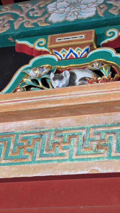       Close-up of a colorful wooden carving of a sleeping cat surrounded by ornate floral details.
  