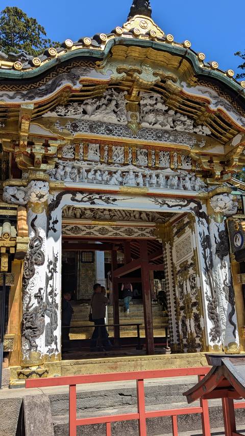       Elaborately carved and gold-trimmed shrine gate with intricate reliefs under bright daylight.
  