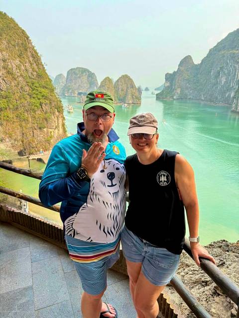       Smiling couple posing at a high viewpoint overlooking emerald waters and limestone karsts
  
