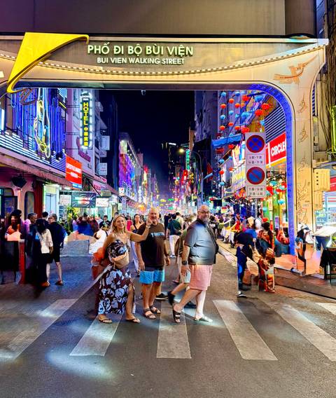       Colorful neon-lit nightlife street packed with crowds and lanterns, with friends posing in the foreground
  
