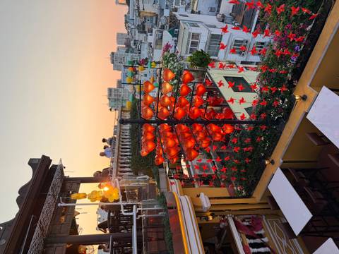       Rooftop café adorned with red lanterns at golden sunset overlooking city buildings
  