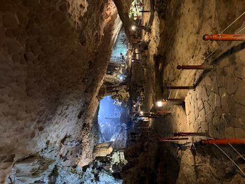       Illuminated walkway descending into a vast limestone cave chamber with visitors in the distance
  