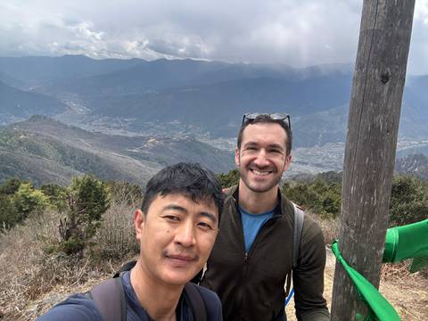       Two hikers taking selfie on mountain viewpoint overlooking broad Bhutan valley
  